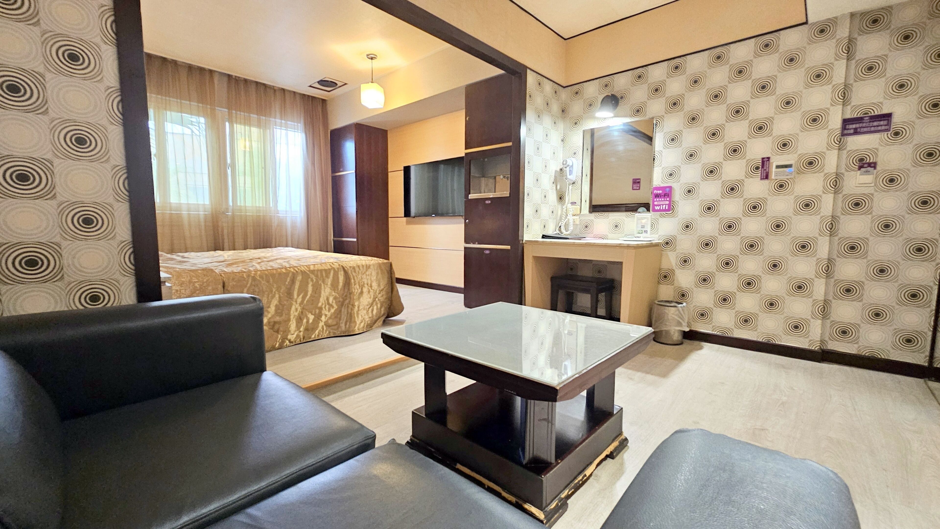 Una habitación de hotel con cama, sofá, una mesita, espejo, kitchenette y pared con diseño.