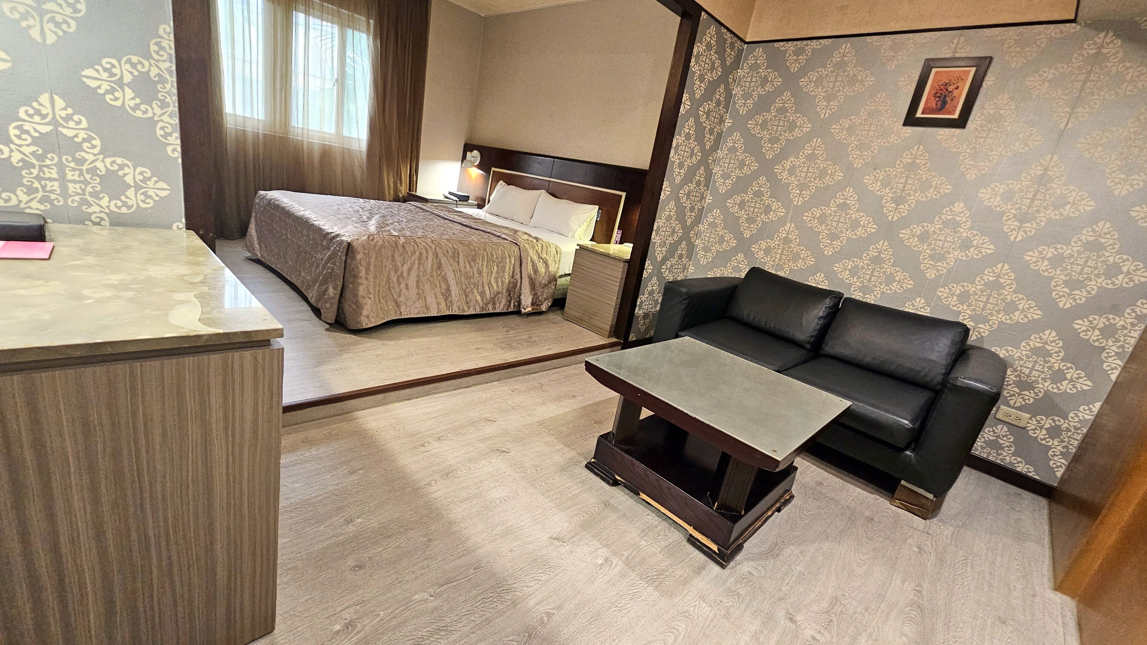 A hotel room with a bed, a black leather sofa, a small table, and a desk.