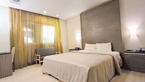 A hotel room with a bed, a desk, a chair, a nightstand, and a window with curtains. - Beckham Motel (Taoyuan City)
