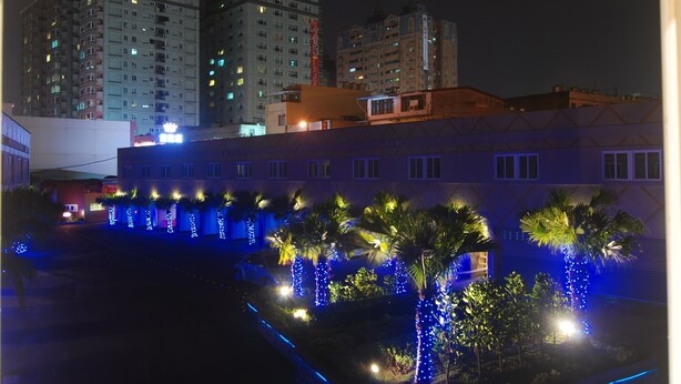 A nighttime view of a building with multiple floors, illuminated windows, and a parking area with a car. - Beckham Motel (Taoyuan City)