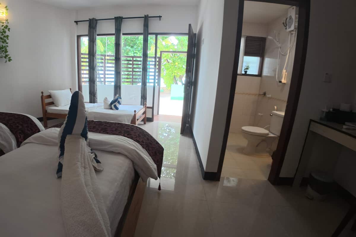 A hotel room with two beds, a bathroom, and a view of the outdoors.