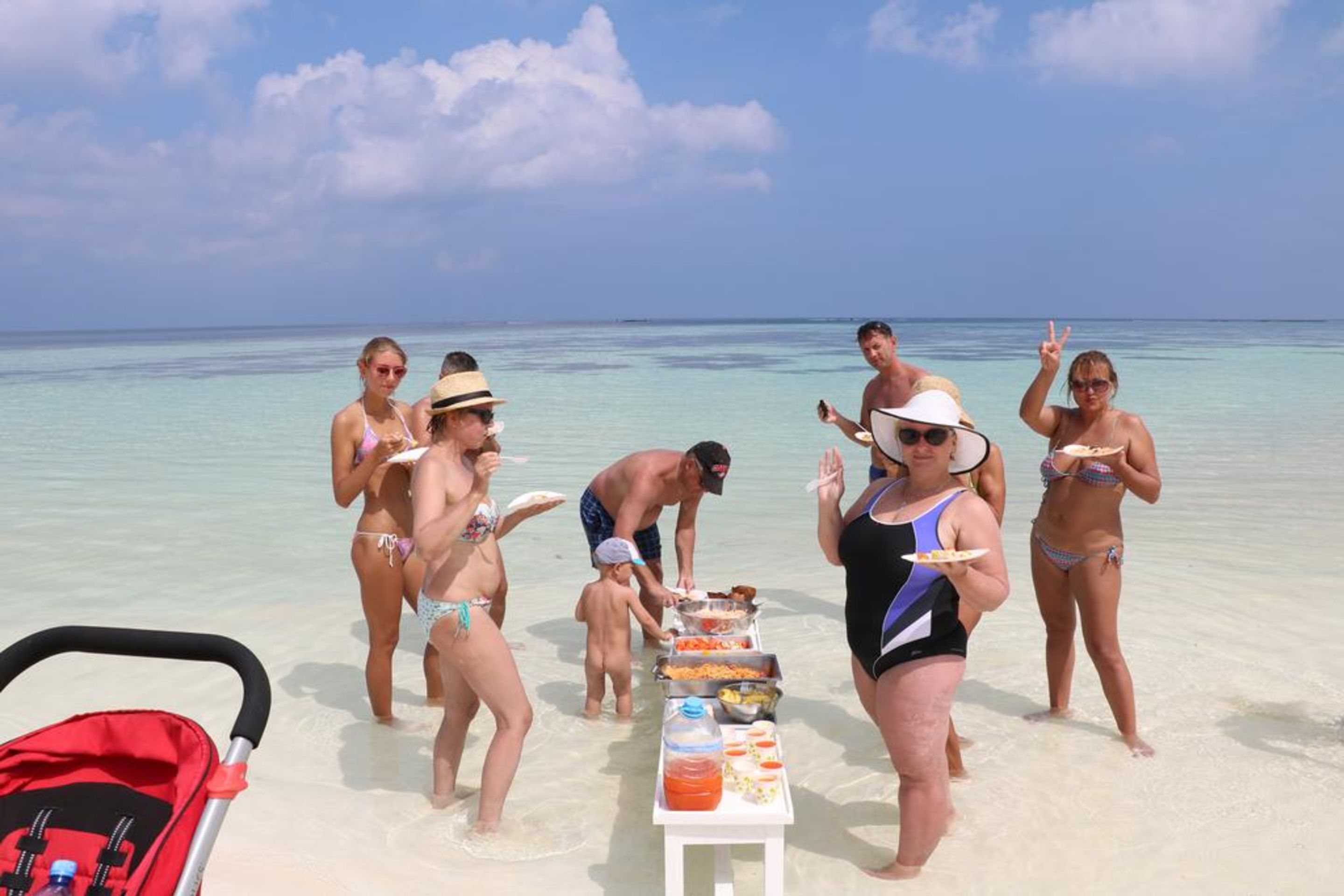 A group of people on a beach with a table of food and drinks.