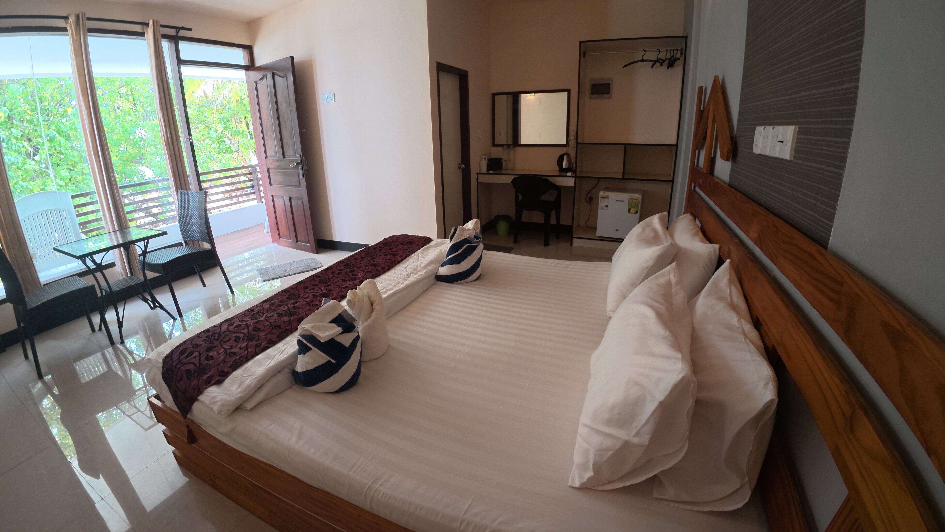 A hotel room with a bed, a desk, a chair, and a balcony with a view of greenery.