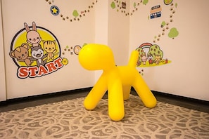A yellow inflatable figure in a room with patterned carpet and wall decorations including a 'START' sign and cartoon characters. - Morn Sun Hotel (Yuanlin)