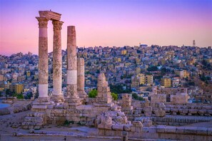 Ancient ruins with columns, set against a cityscape at sunset.