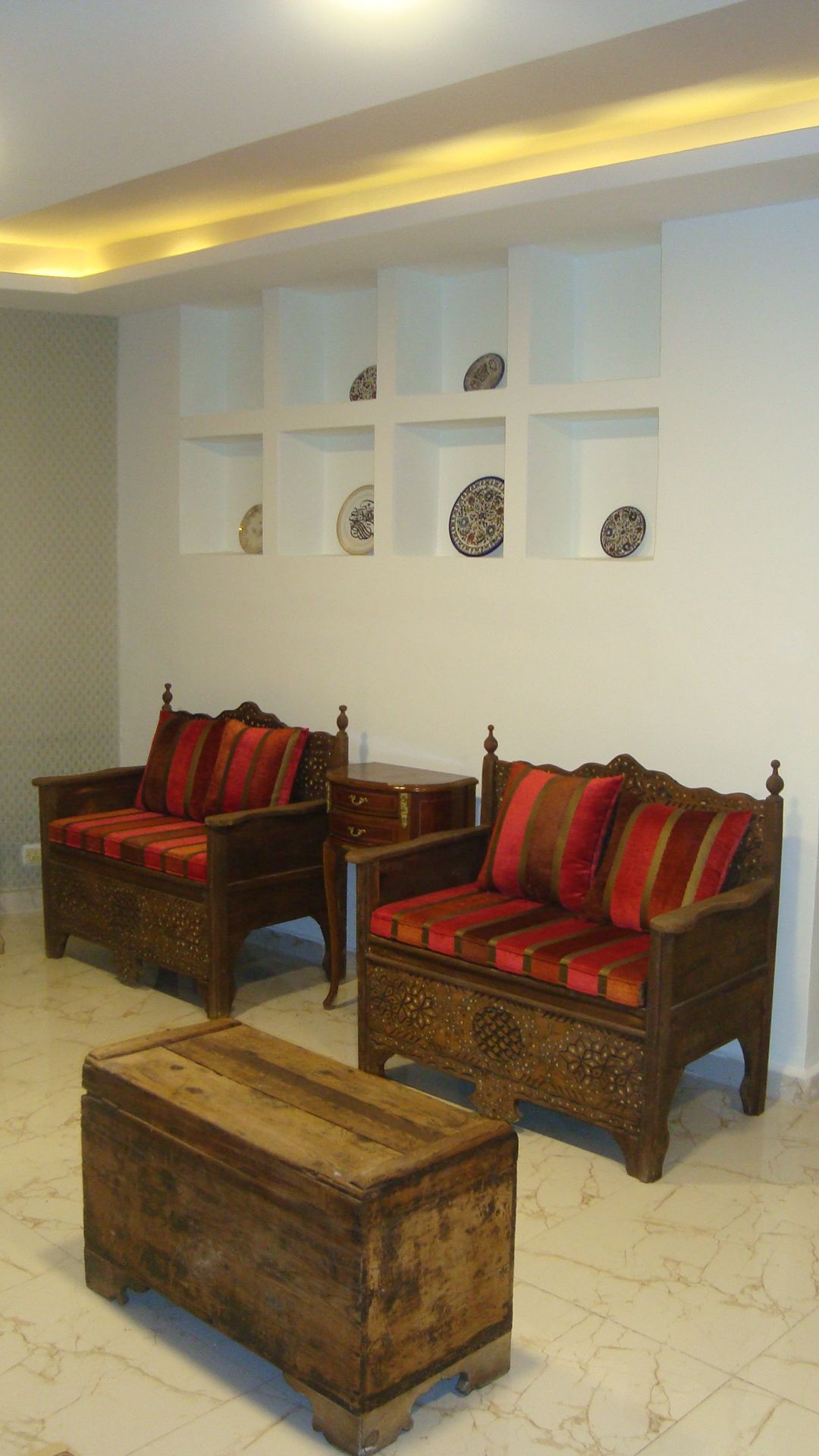 Quarto com dois sofás de madeira com almofadas vermelhas, uma mesa de centro de madeira e uma parede com pratos decorativos.