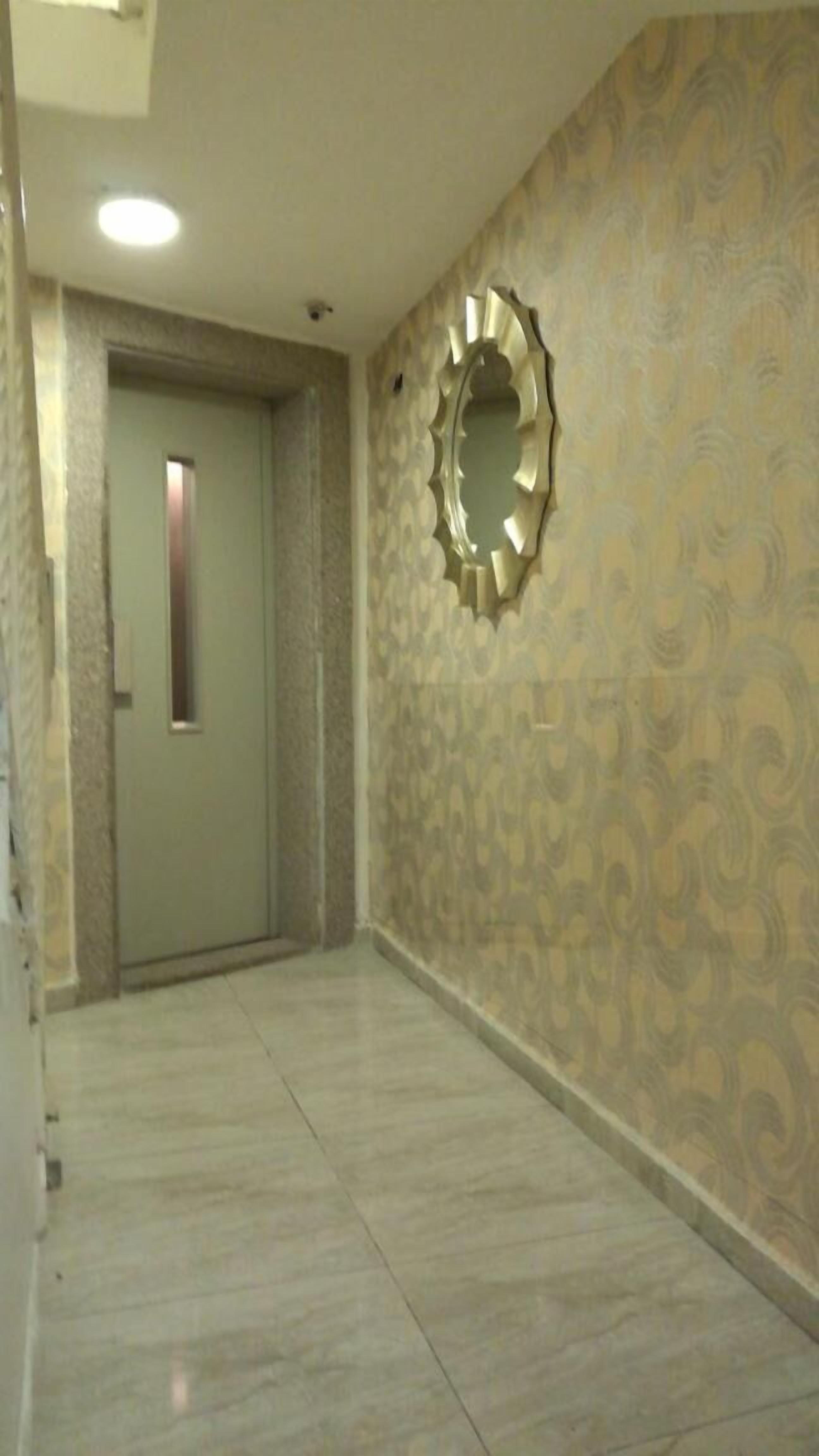 Un pasillo con papel tapiz estampado, una puerta y un espejo fijado a la pared.