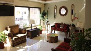 A living room with a sofa, a coffee table, and a TV. There are plants and a window with a view. - Rafi Hotel Amman (Amman)