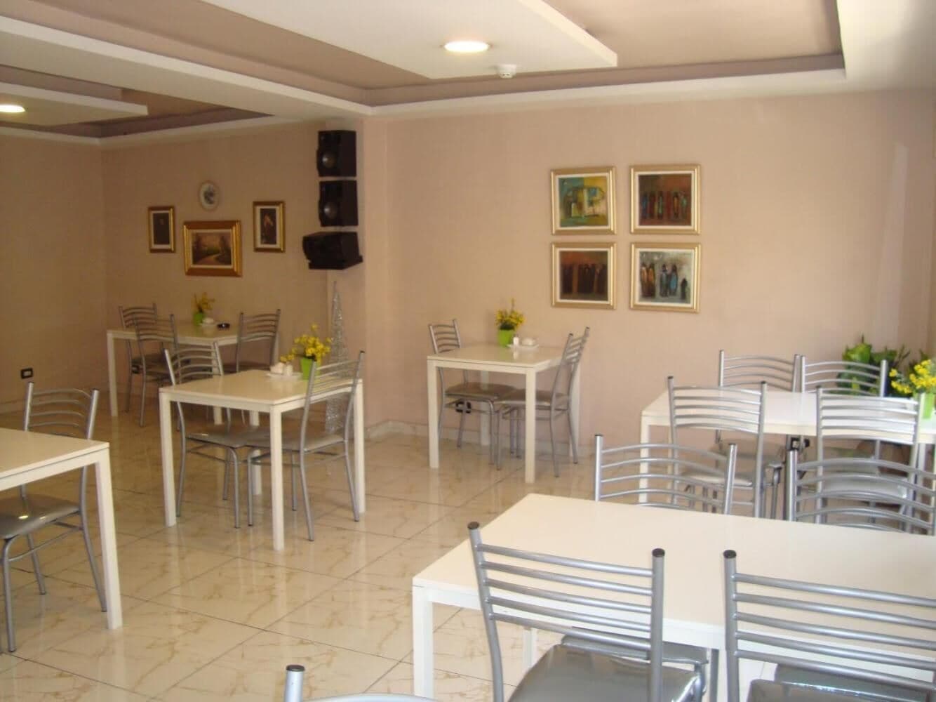 Un comedor con varias mesas y sillas, dispuesto en una sala amplia con paredes color crema y piso de baldosas.