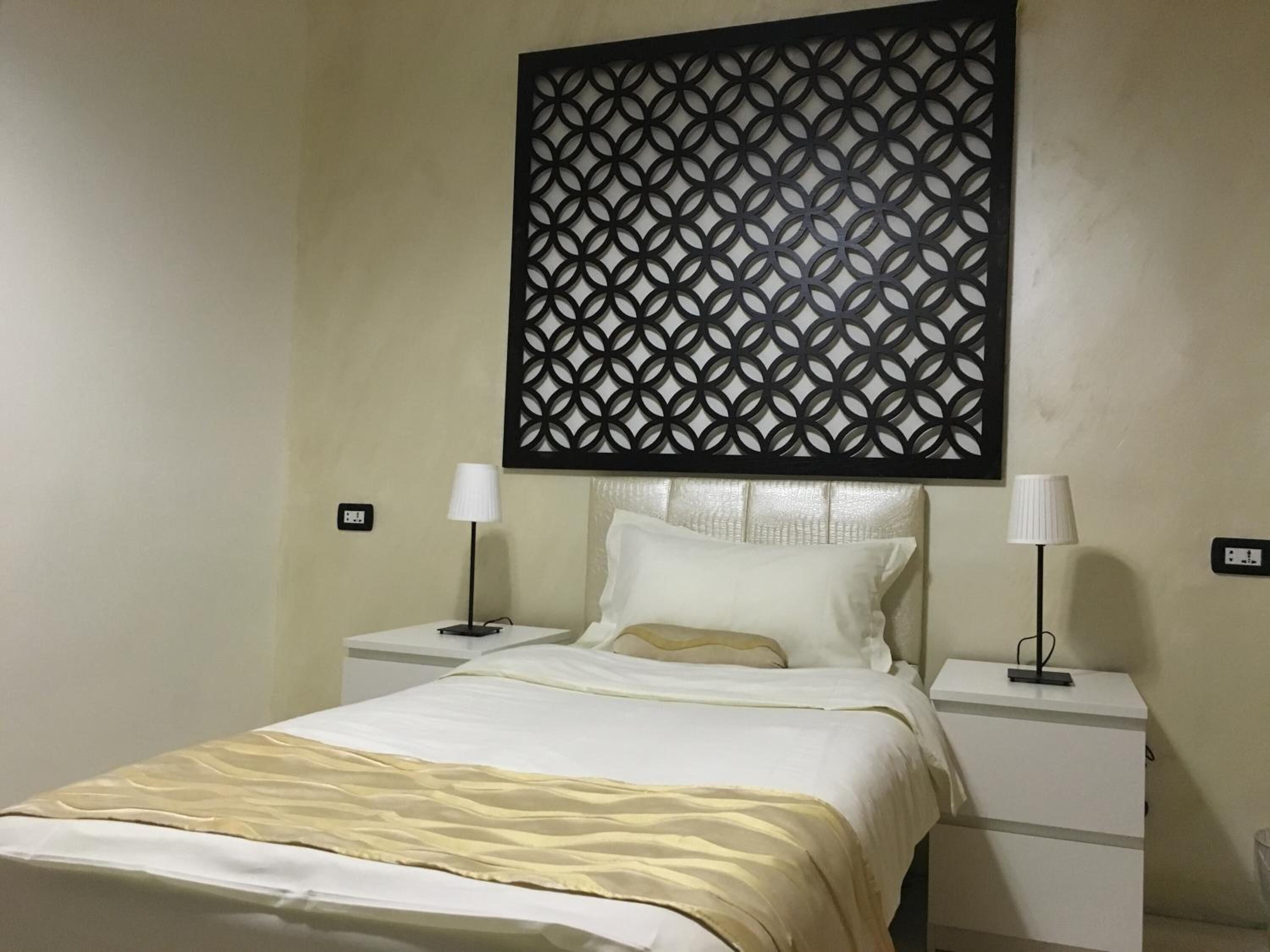 A hotel room with a bed, two bedside tables, a decorative wall panel, and two wall-mounted lamps.