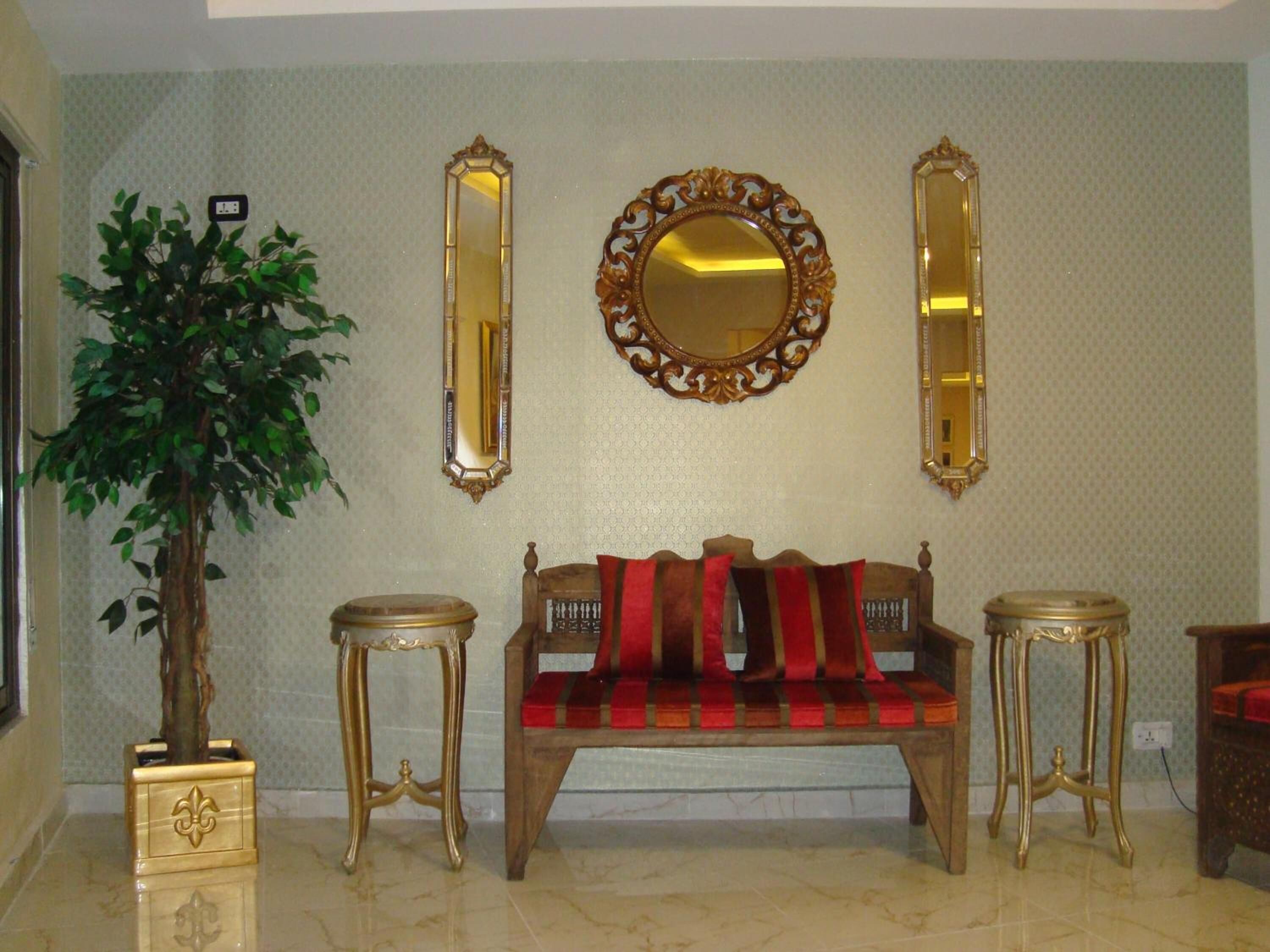 A room with a wooden bench, two gold-framed mirrors, and a potted plant.