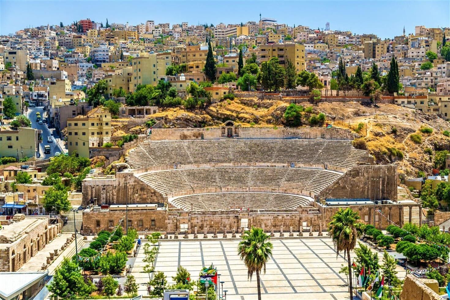 Un anfiteatro antiguo rodeado de edificios modernos y vegetación.