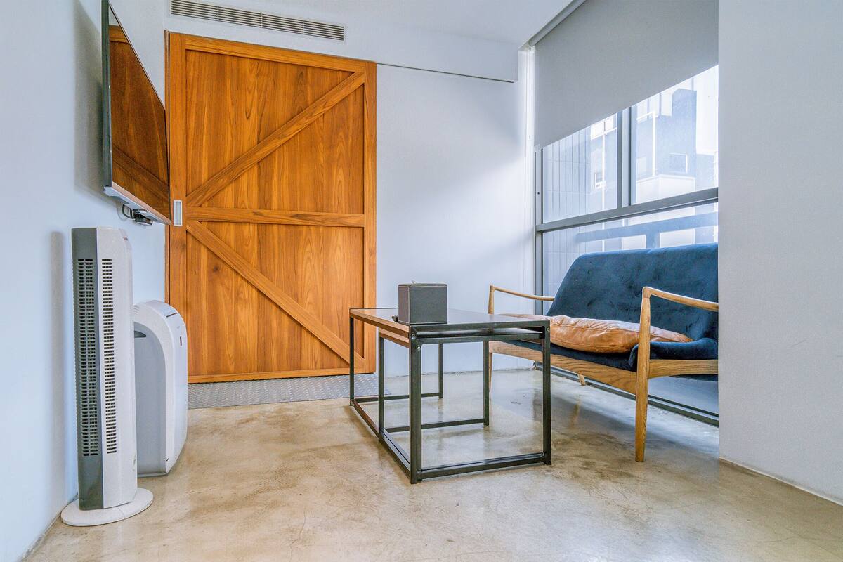 A room with a wooden sliding door, a table with a laptop, a blue sofa, and two standing fans.