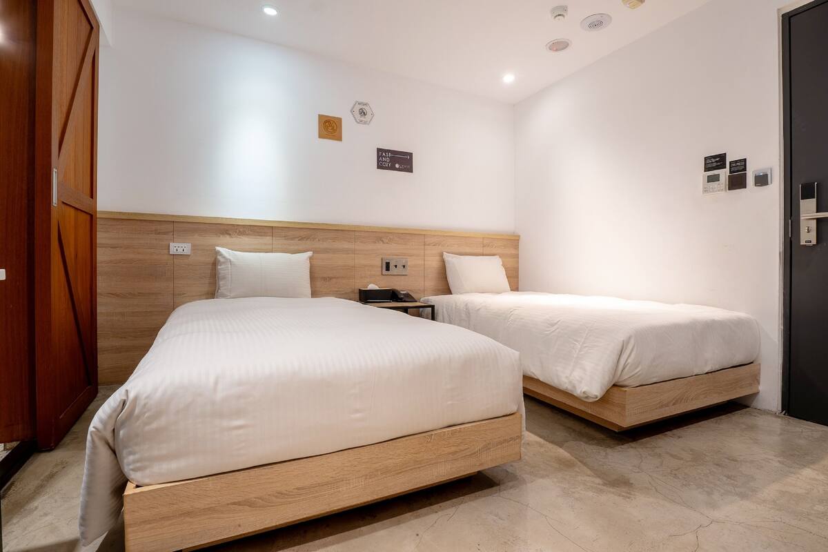 A hotel room with two wooden beds, a wooden wardrobe, a nightstand, and a black door.