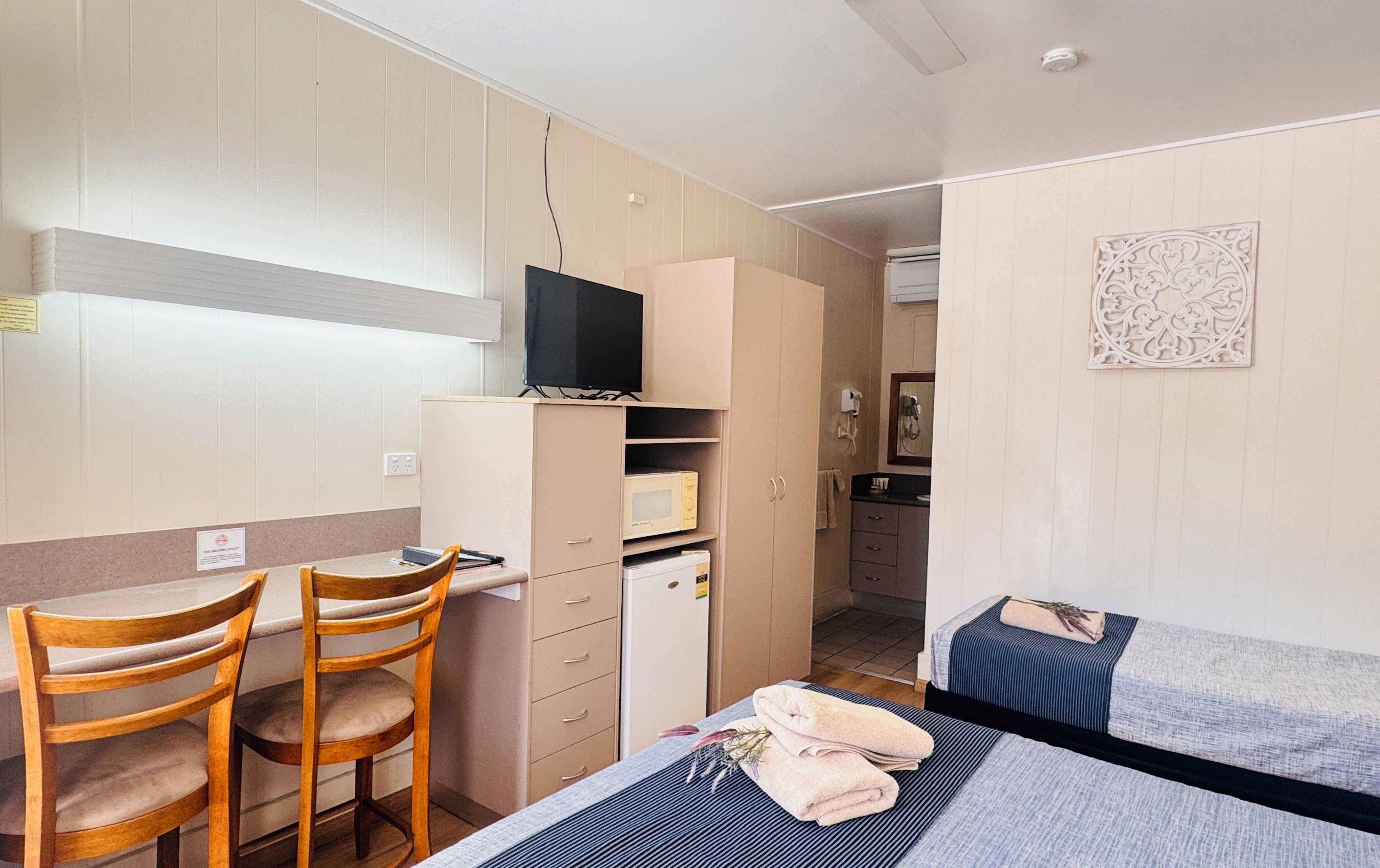 A bedroom with a bed, a desk with a chair, a microwave, and a television.