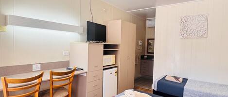 A bedroom with a bed, a desk with a chair, a microwave, and a television.