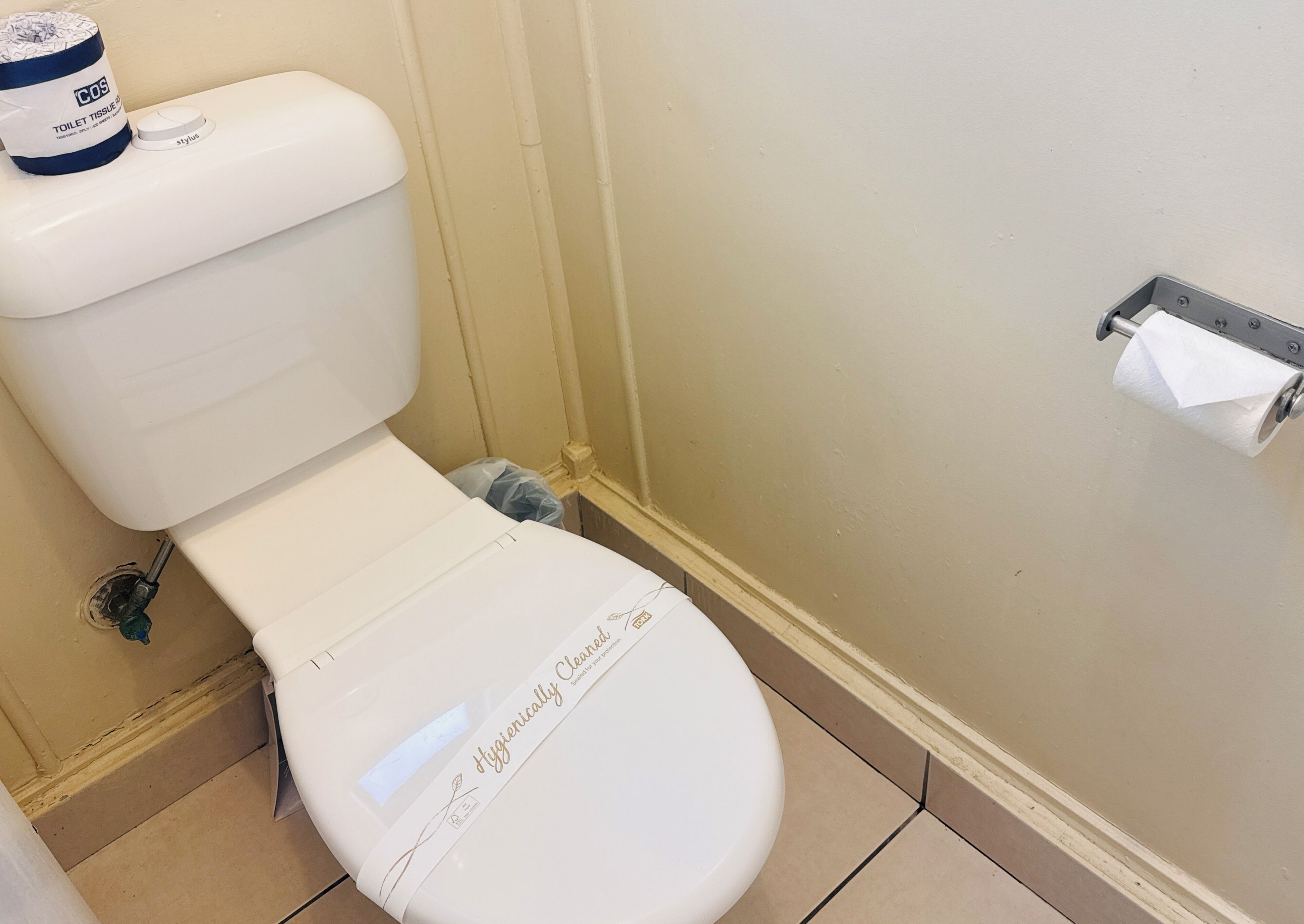 Un inodoro blanco con un rótulo que dice 'Hygienically Cleaned', un dispensador de papel higiénico y un rollo de papel en la pared.
