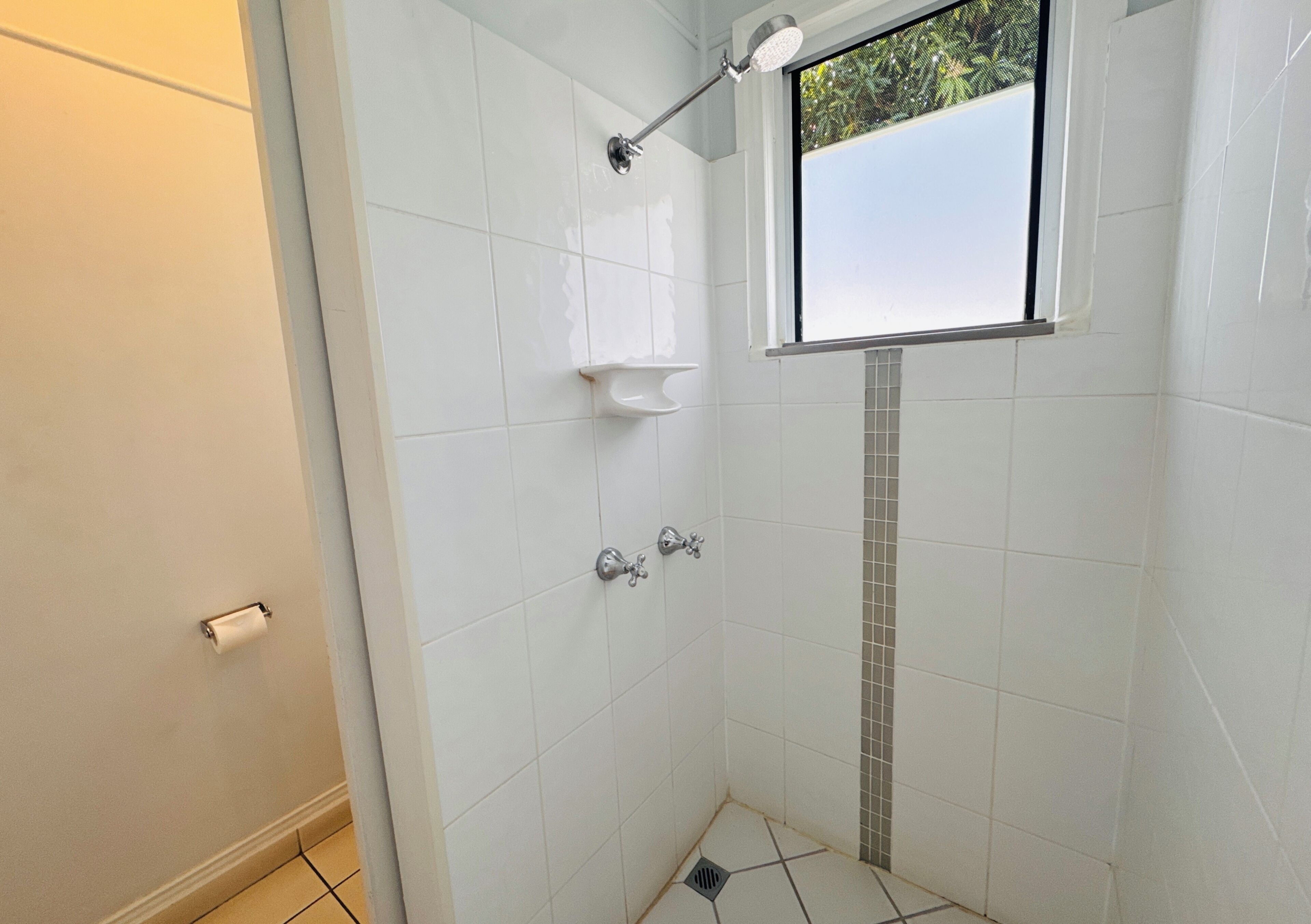 A small, tiled shower area with a window, a towel rack, and a toilet paper holder.