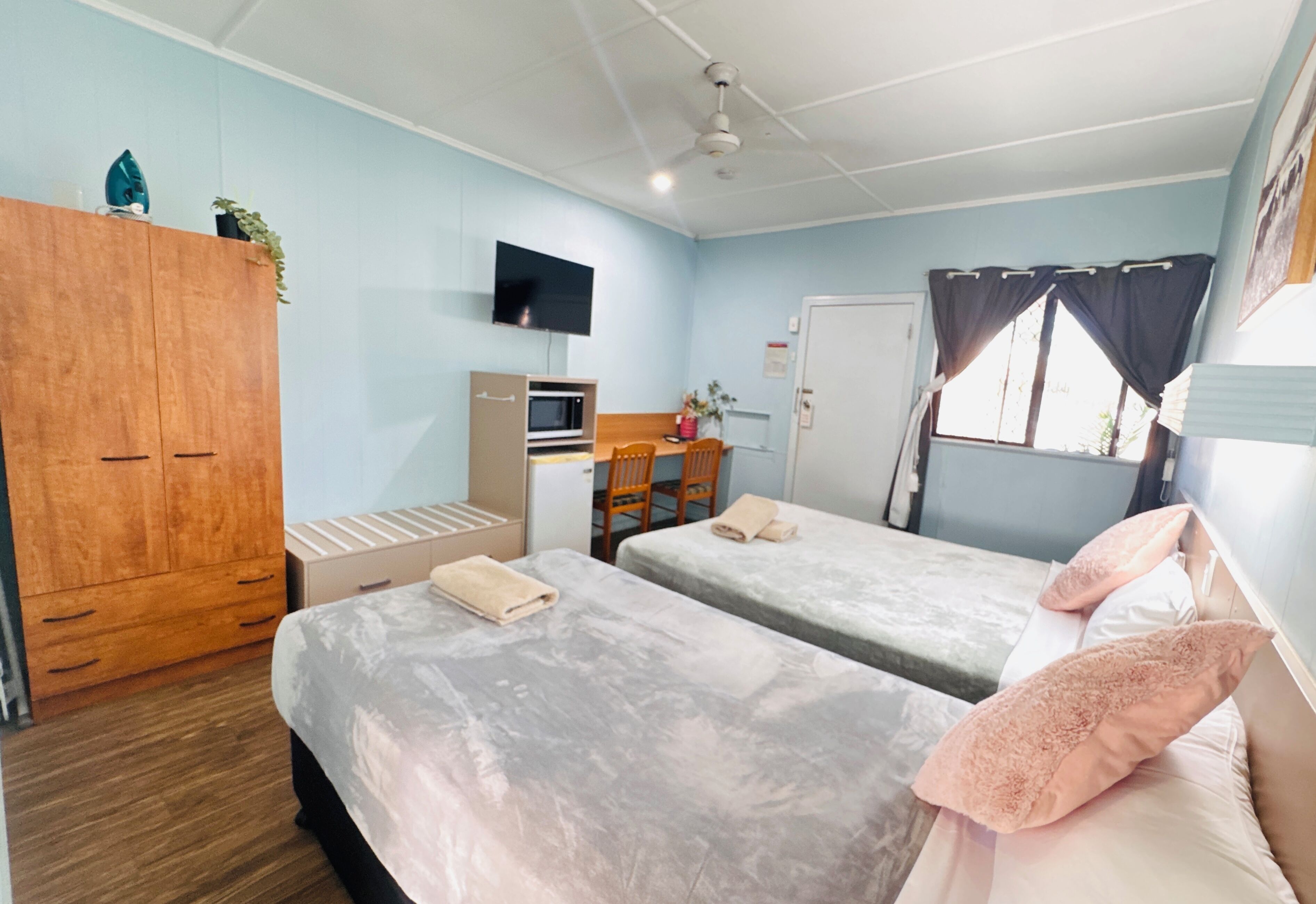 Una habitación con dos camas, un armario de madera, un escritorio con silla, un televisor y una ventana con cortinas.