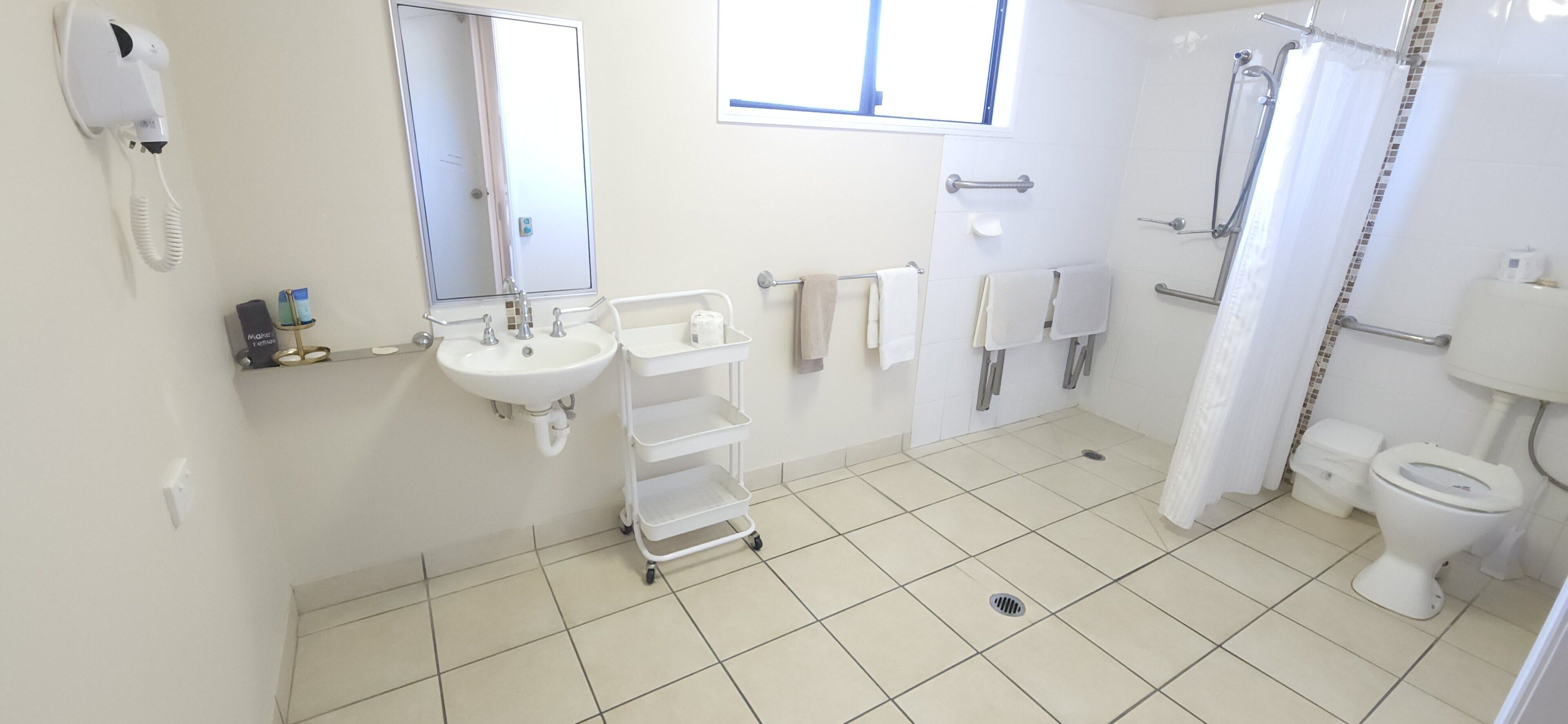 A clean, modern bathroom with a white sink, mirror, and toilet. There is a shower area with a curtain, and towels are neatly hung on a rack.