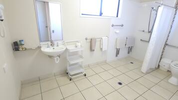 A clean, modern bathroom with a white sink, mirror, and toilet. There is a shower area with a curtain, and towels are neatly hung on a rack.