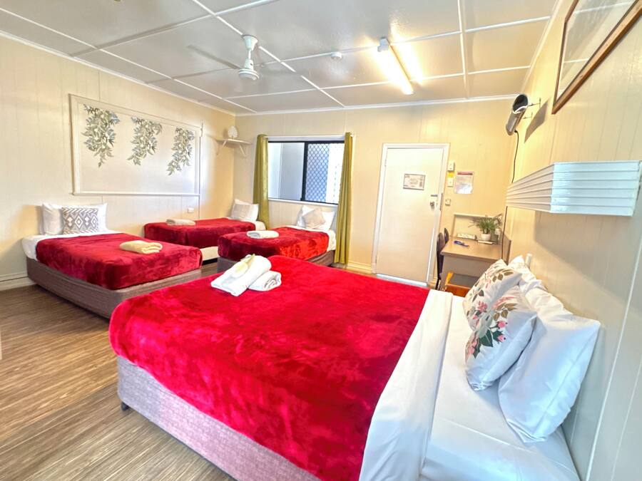 Une chambre d’hôtel avec deux lits, un bureau, une chaise, une fenêtre avec des rideaux et un ventilateur de plafond.