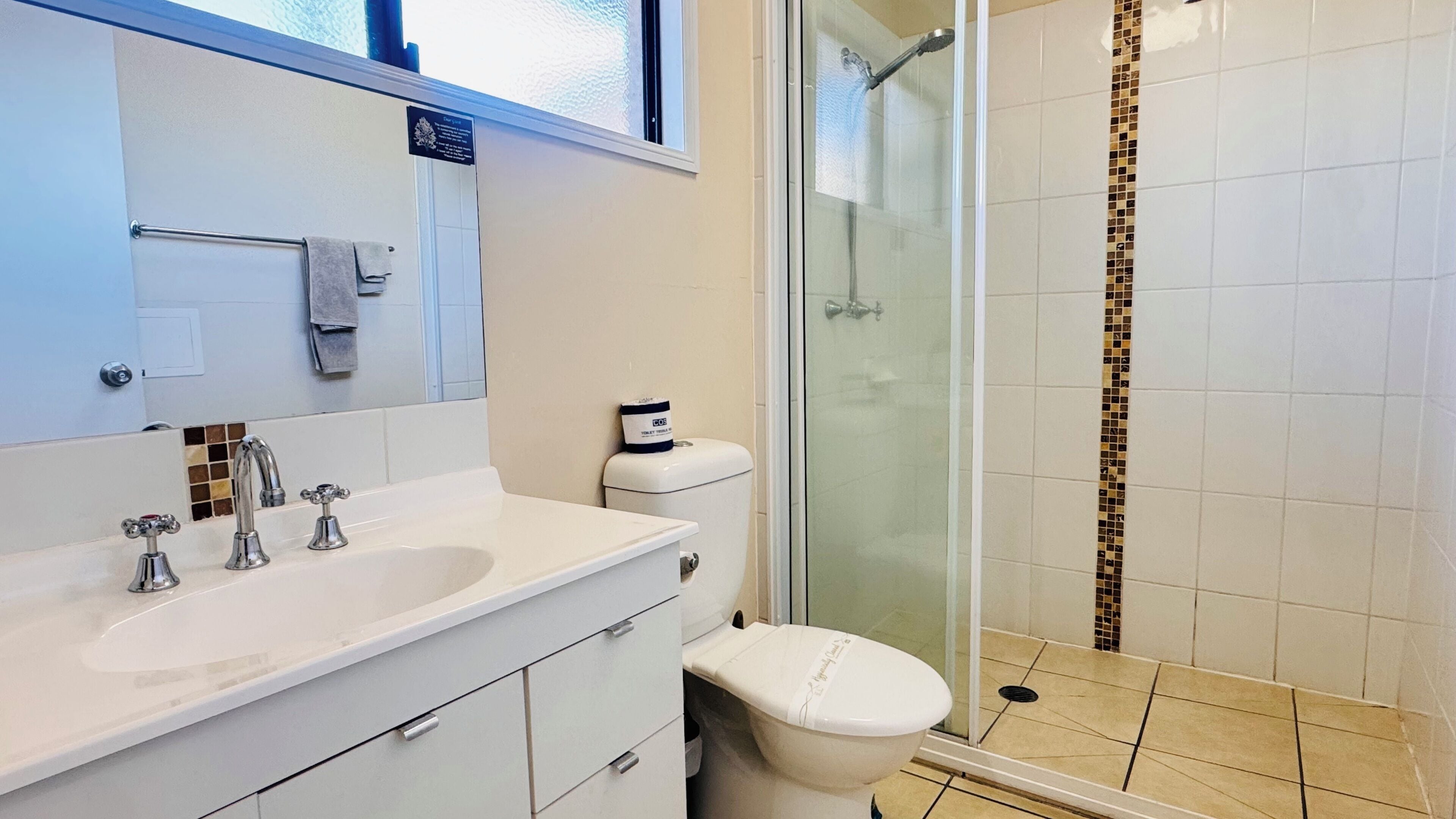 A bathroom with a white sink, two faucets, a toilet, and a glass shower enclosure.