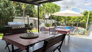 An outdoor patio area with a grill, table, chairs, and a pool.