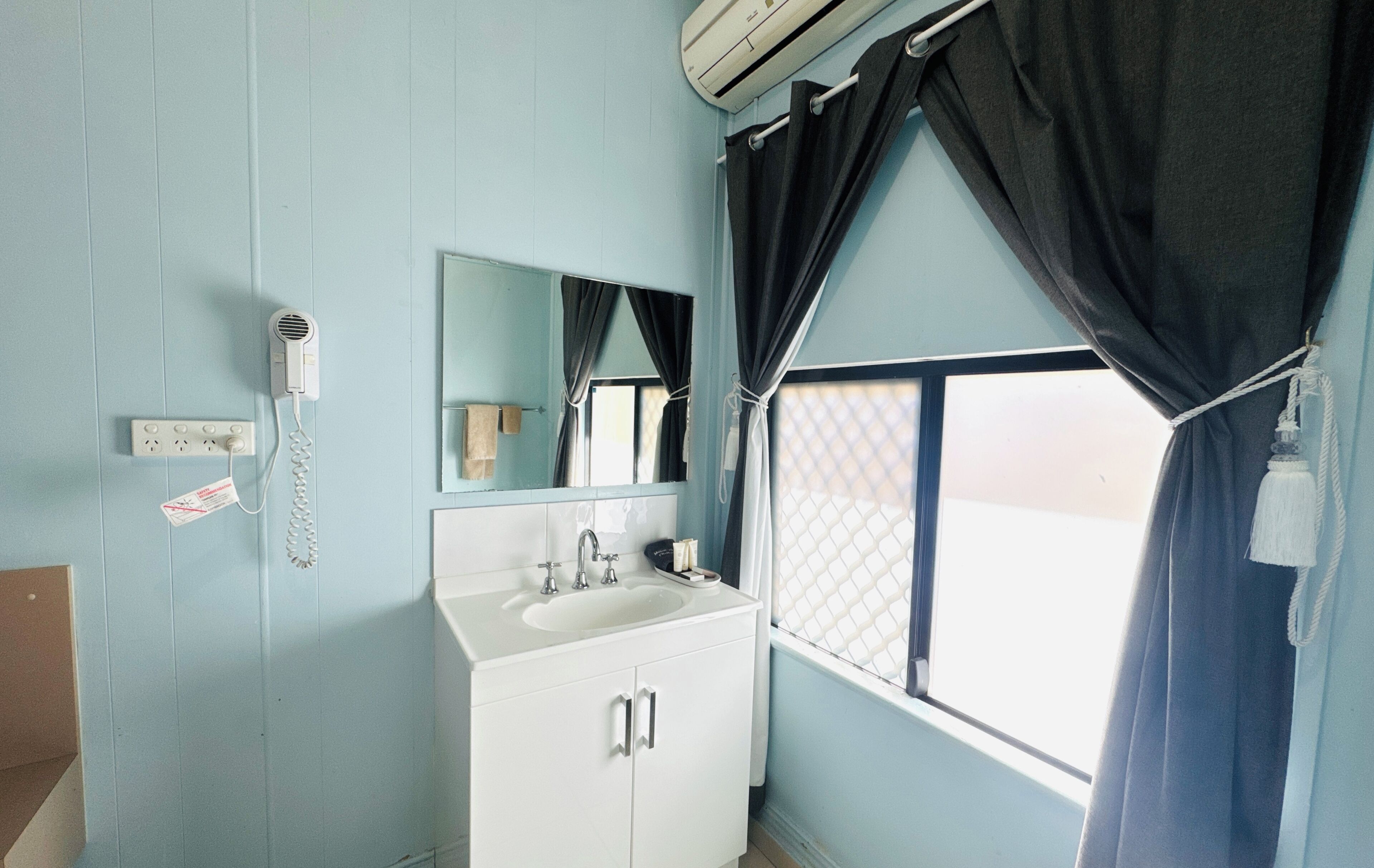 A bathroom with a sink, mirror, and a window with curtains.