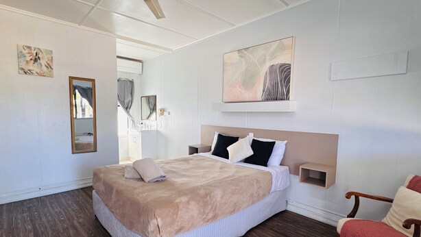 A bedroom with a large bed, a nightstand, a chair, and a painting on the wall.