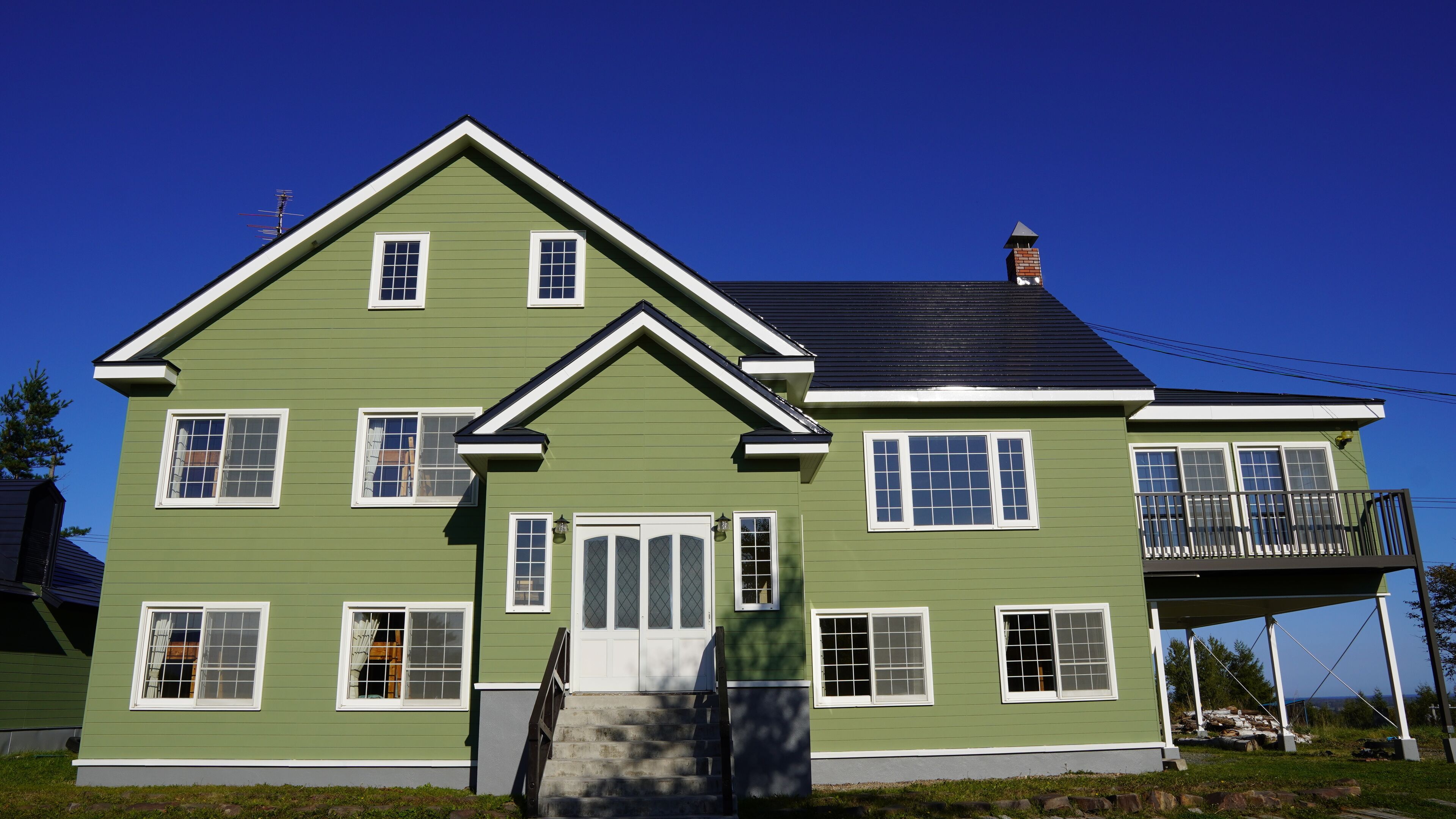 A two-story house with a green exterior, white trim, and a balcony on the second floor.