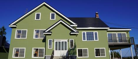 A two-story house with a green exterior, white trim, and a balcony on the second floor.