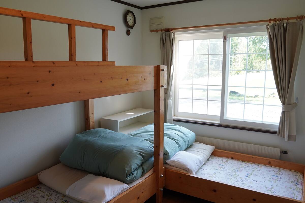 Habitación con literas, cabecera de madera, estante blanco y ventana con cortinas.