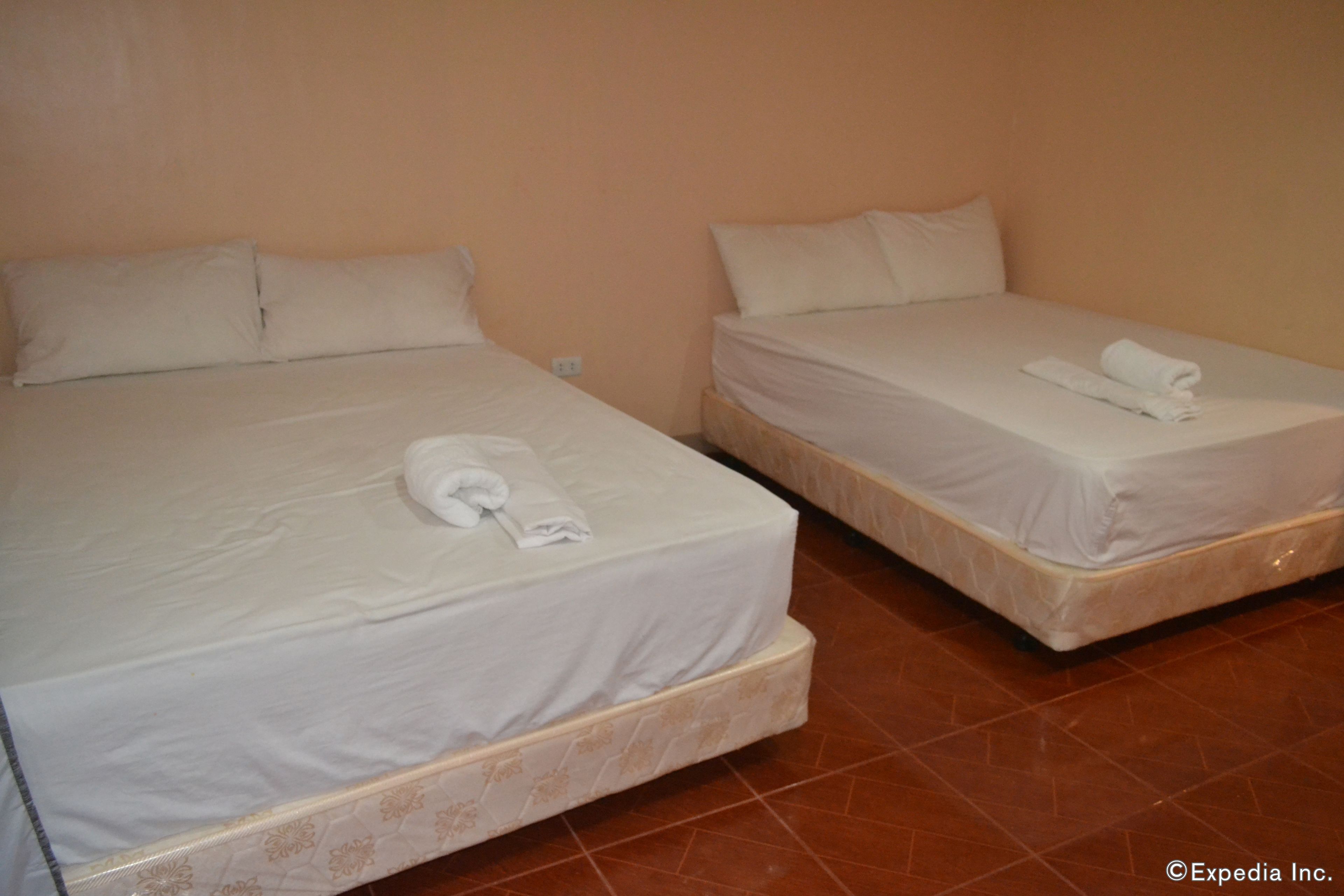 Two single beds with white linens and towels, a tiled floor, and a plain wall.