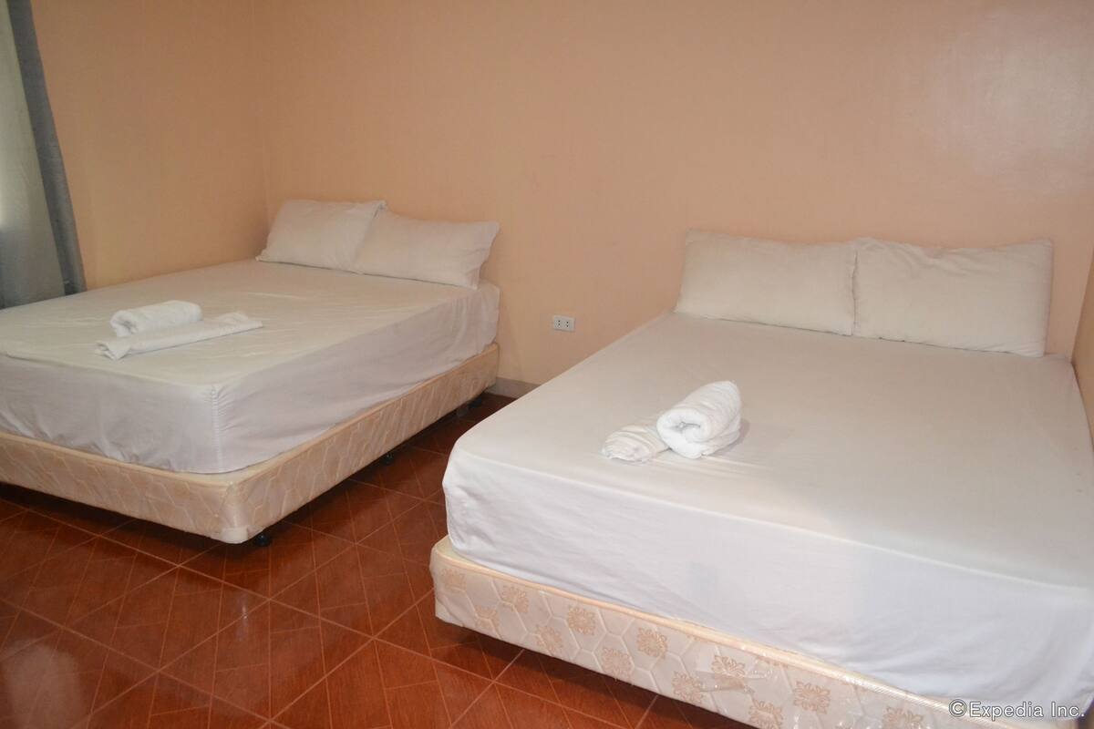 Two single beds with white linens and pillows, a tiled floor, and a plain wall.