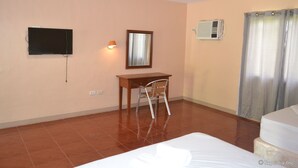 A hotel room with a bed, a desk with a chair, a television mounted on the wall, and an air conditioning unit. - Amandari Cove (General Santos)