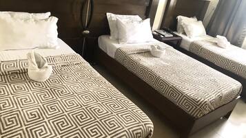 A hotel room with two single beds, each with a patterned bedspread and white pillows. There is a bedside table with a lamp and a phone.