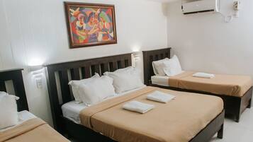 A hotel room with two single beds, a ceiling fan, an air conditioning unit, and a colorful painting on the wall.