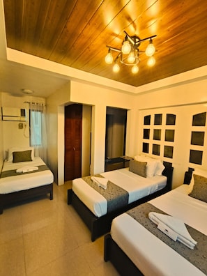 Habitación de hotel con tres camas, techo de madera y una lámpara moderna.