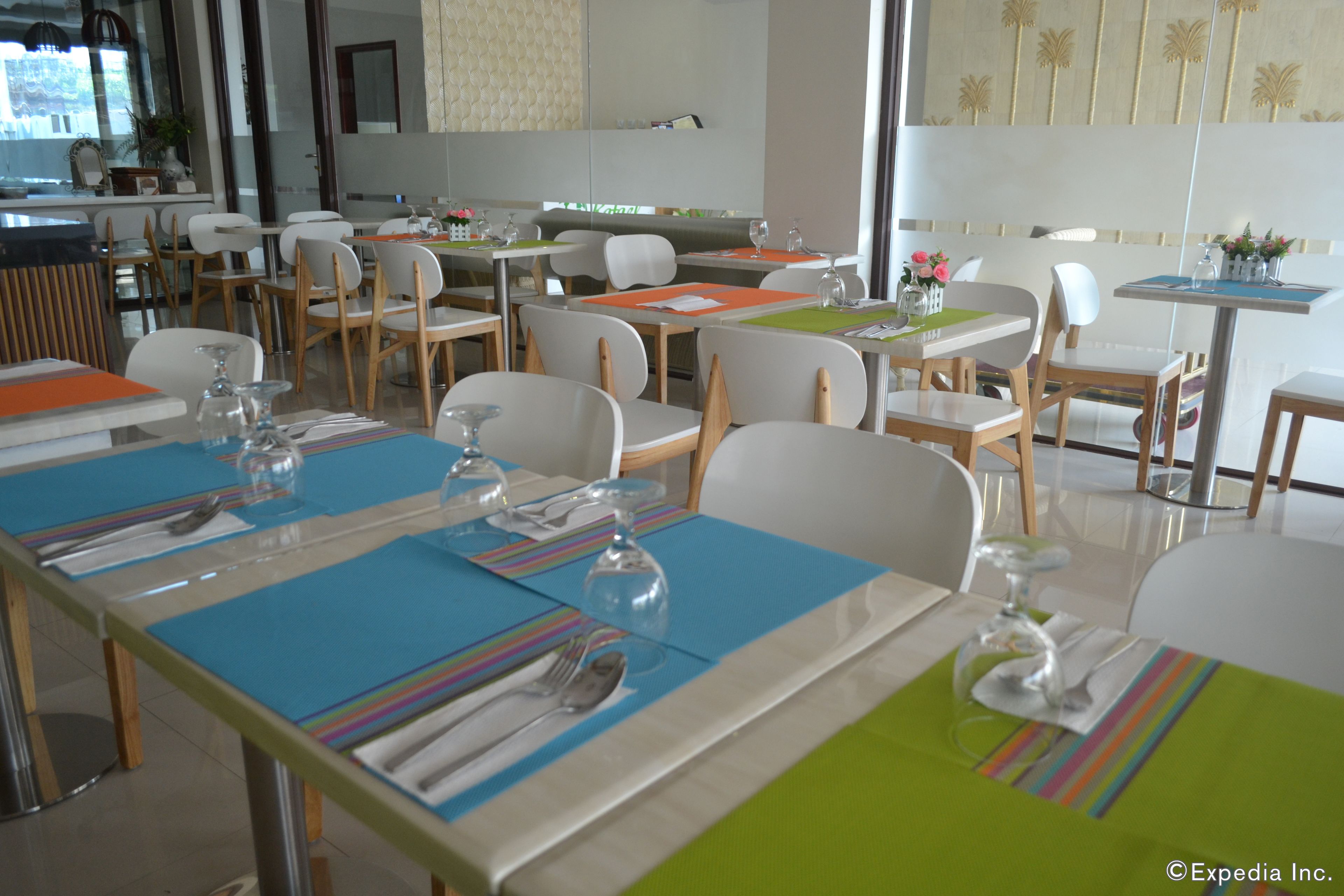 A dining area with tables set for two, equipped with cutlery and wine glasses, and a view of the city through large windows.