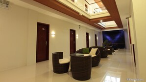 Un hall d’hôtel moderne avec un plafond haut, un atrium en verre et un espace détente doté de meubles en osier.