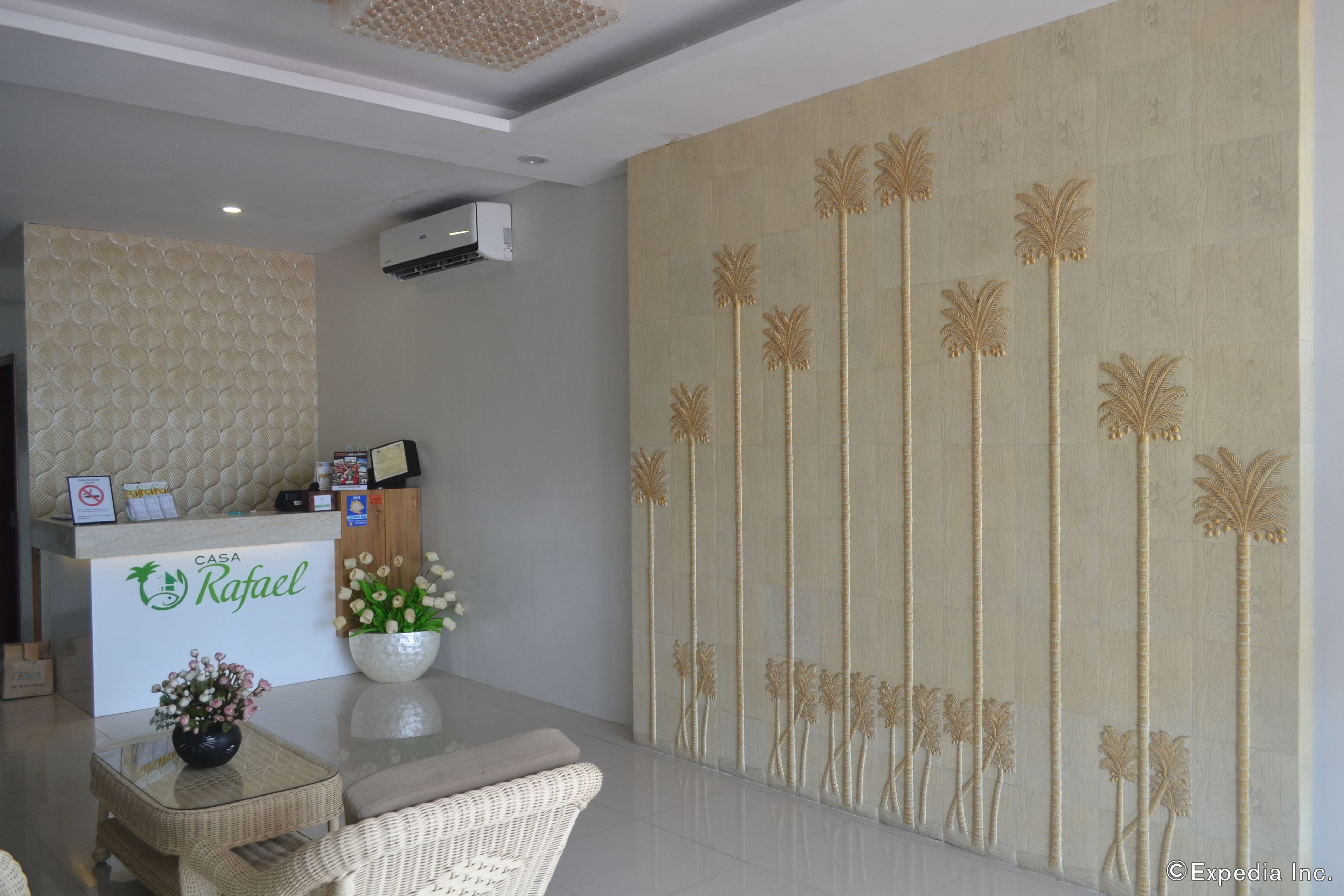 A reception area with a reception desk, a wall with palm tree designs, and a flower vase.