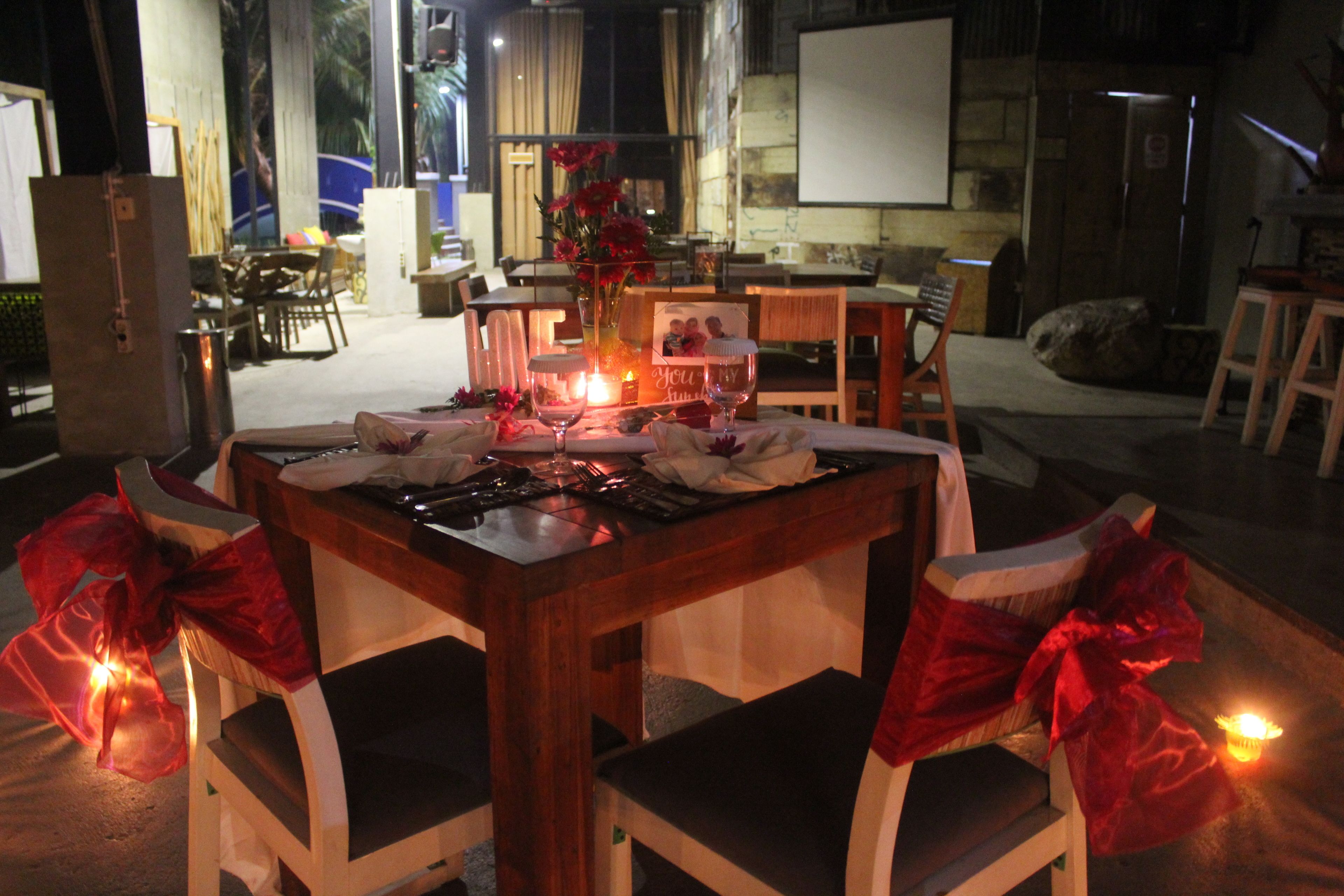 A dining area with a table set for two, surrounded by chairs with red bows.