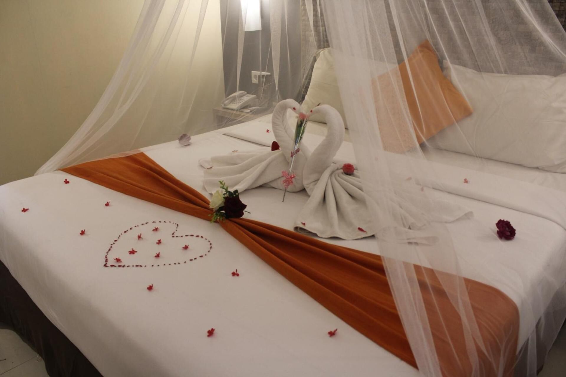 Una cama cuidadosamente tendida con un diseño en forma de corazón, un ramo de flores y una decoración de toallas en forma de cisne.