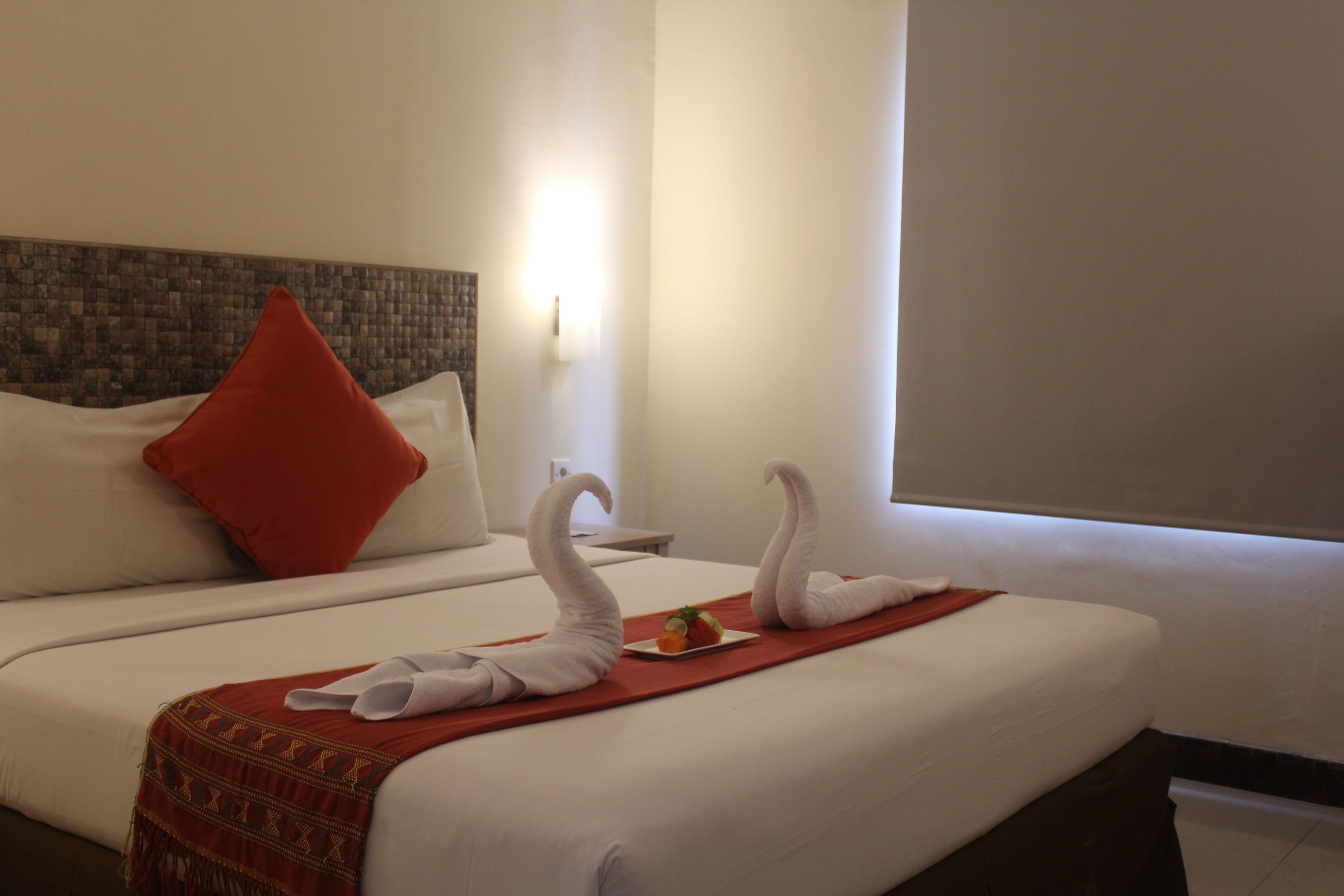 A hotel room with a large bed, a red pillow, and two swan-shaped towels on the bed.