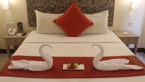 A hotel room with a neatly made bed, a red pillow, and two swan-shaped towels on the bed. - Greenotel Cilegon (Cilegon)