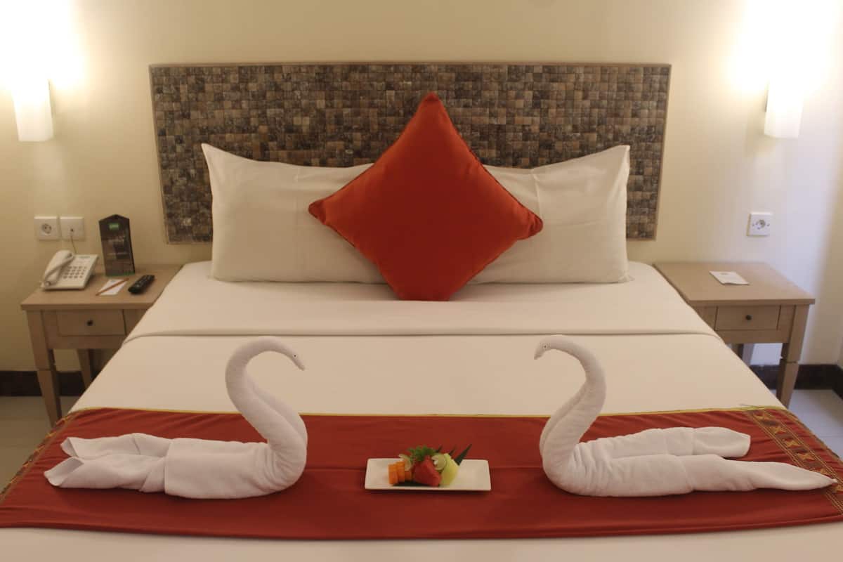 A hotel room with a neatly made bed, a red pillow, and two swan-shaped towels on the bed.