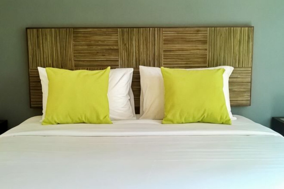 A bed with white and green pillows, a wooden headboard, and a plain wall.