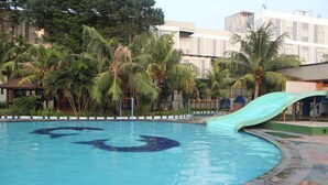 A swimming pool with a slide, surrounded by palm trees and buildings. - Greenotel Cilegon (Cilegon)