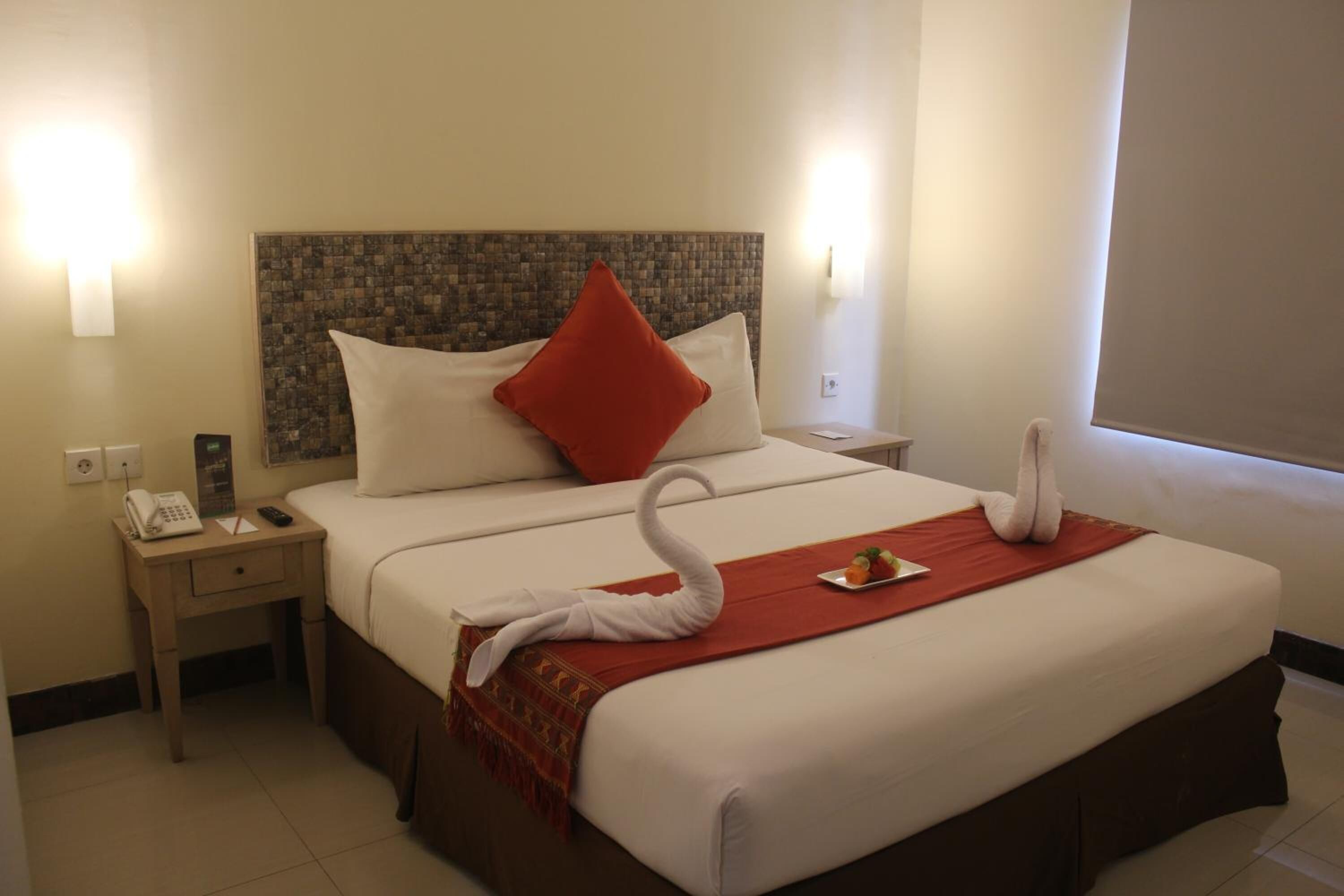 Una habitación de hotel con una cama bien hecha, un teléfono en la mesita de noche y una decoración de toalla con forma de cisne.